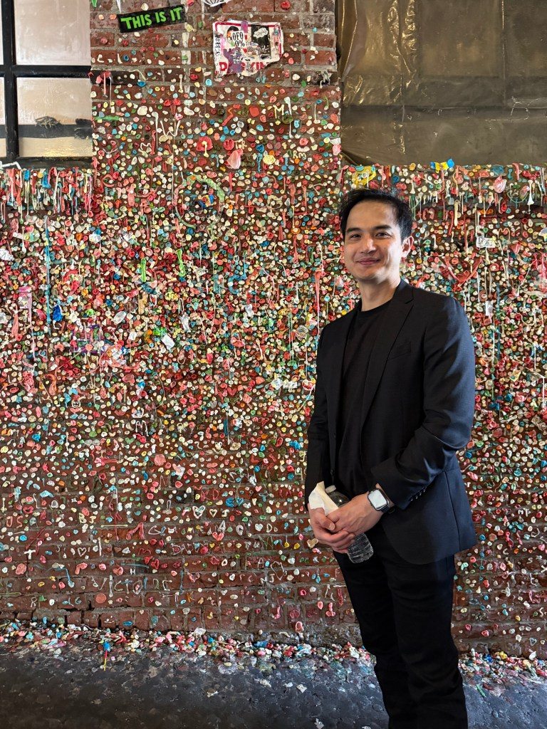 Person standing in front of the Gum Wall, a colorful display covered in chewing gum at Pike Place Market in Seattle.